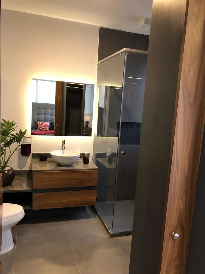 Baño con mueble de madera y espejo iluminado — casa residencial construida por Prisma Habita en Puebla