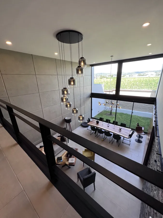 Comedor a doble altura con lámparas colgantes y vista — casa residencial construida por Prisma Habita en Puebla