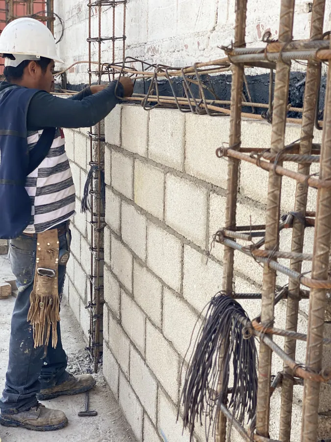 Obrero levantando muro de block junto a castillo de acero — proceso de construcción de casa residencial en Puebla