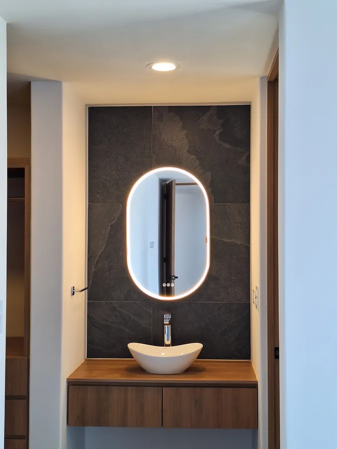 Baño de cortesía con espejo oval retroiluminado y piedra — casa Missouri 99 en el corredor Angelópolis, Puebla