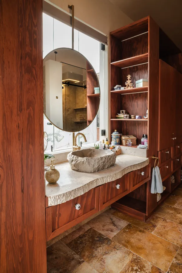 Baño con lavabo de piedra, mueble de madera y espejo circular — casa residencial de autor en Atlixco, Puebla