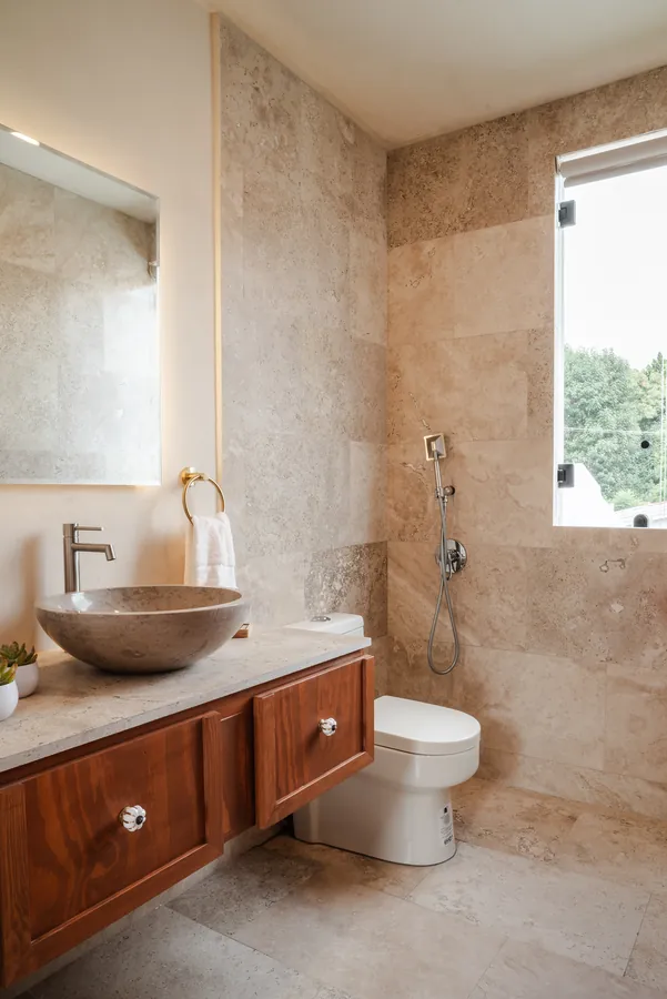 Baño de visitas con muros de piedra y lavabo tallado — casa residencial de autor en Atlixco, Puebla